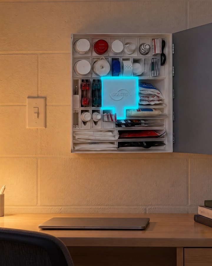 A residence hall room in the evening, the Solstis cabinet open and lit on the wall above the desk